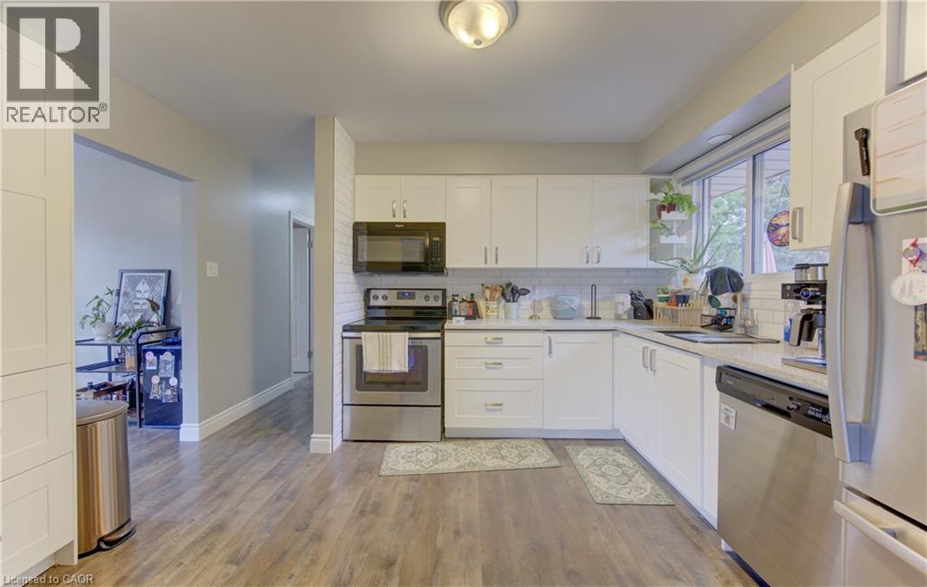 Contemporary kitchen featuring wood-finish flooring, white cabinetry, stainless steel appliances, a subway tile backsplash, and a window above the sink - 127 Strathcona Crescent, Kitchener, ON