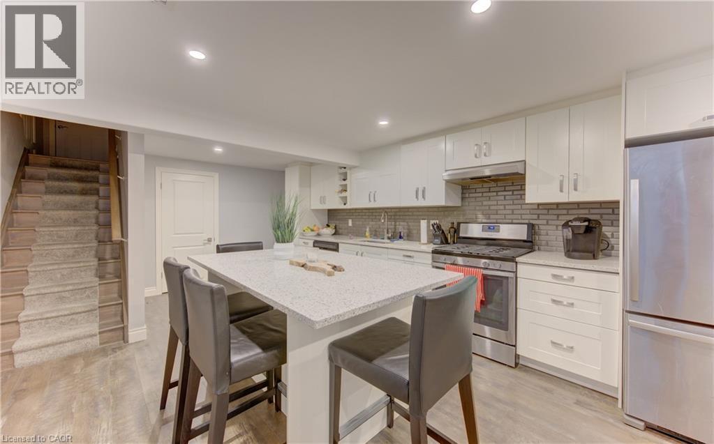 Contemporary kitchen featuring white cabinetry, stainless steel appliances, a light-toned brick-patterned backsplash, and a central island with a light granite-style countertop - 127 Strathcona Crescent, Kitchener, ON