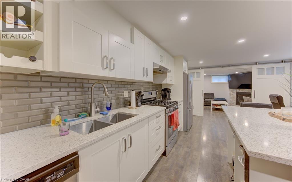 Modern kitchen featuring white shaker cabinetry, stainless steel appliances, a double basin sink, and a light-toned brick-patterned tile backsplash - 127 Strathcona Crescent, Kitchener, ON
