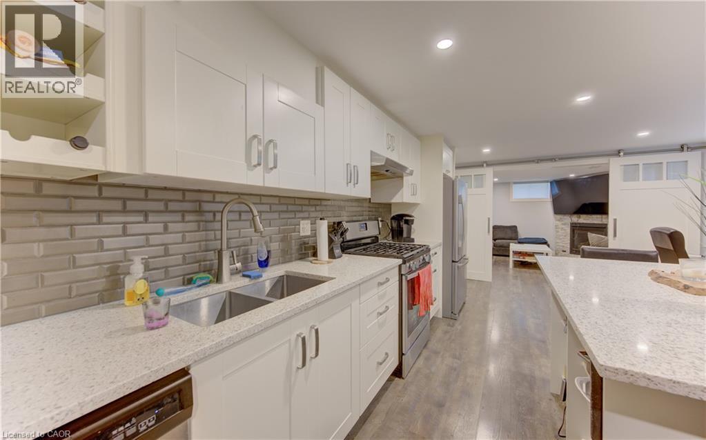 Kitchen featuring white shaker-style cabinetry, light speckled countertops, a double stainless steel sink, and a gray subway tile backsplash - 127 Strathcona Crescent, Kitchener, ON
