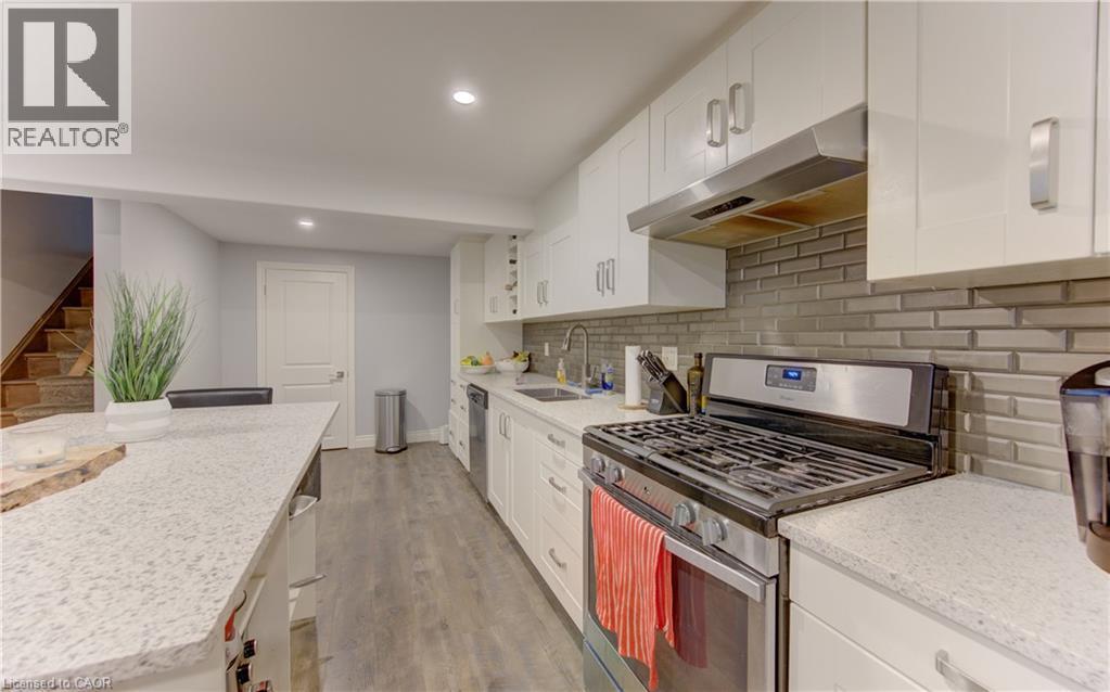 Kitchen featuring a large island with a light-toned countertop, stainless steel appliances, a subway tile backsplash, white cabinetry, and wood-finish flooring - 127 Strathcona Crescent, Kitchener, ON