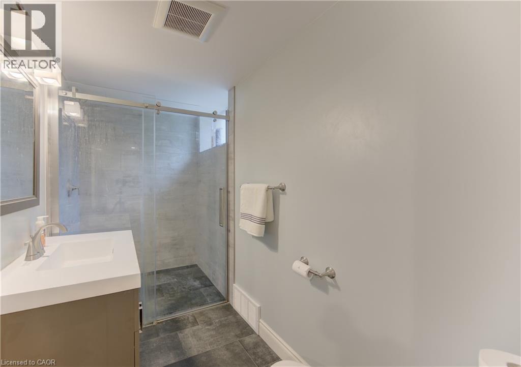 Bathroom featuring a glass-enclosed shower with gray tiled walls and dark floor tiles - 127 Strathcona Crescent, Kitchener, ON