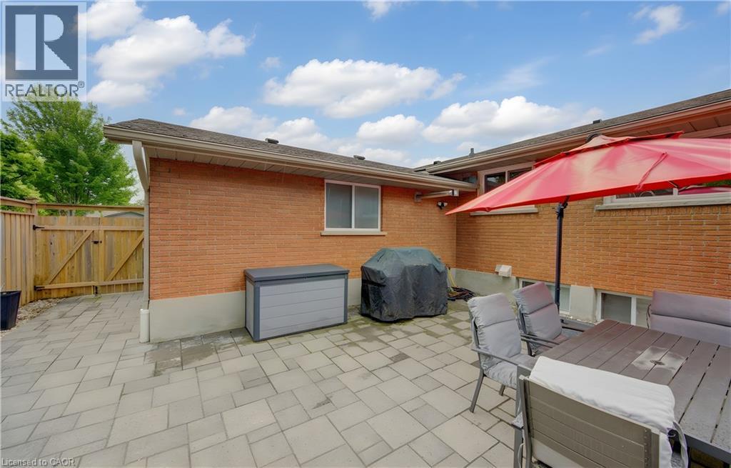 Expansive rear patio featuring a paver stone surface, brick exterior, wood privacy fencing, and multiple windows - 127 Strathcona Crescent, Kitchener, ON