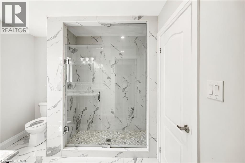 Walk-in shower featuring a glass enclosure, white marble-style wall tiling, and a pebble-stone floor - 129 St George Street, Kitchener, ON