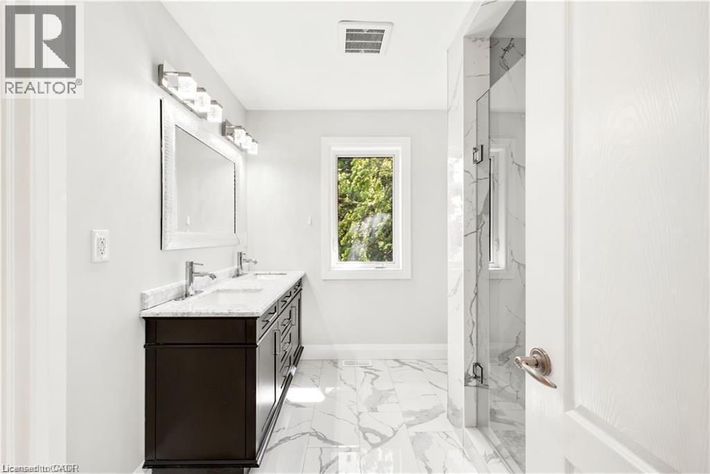 Bathroom featuring a double vanity with a dark wood-finish cabinet and light-toned countertop, a shower enclosure with floor-to-ceiling tile, white tile flooring, a single window, and bright overhead - 129 St George Street, Kitchener, ON