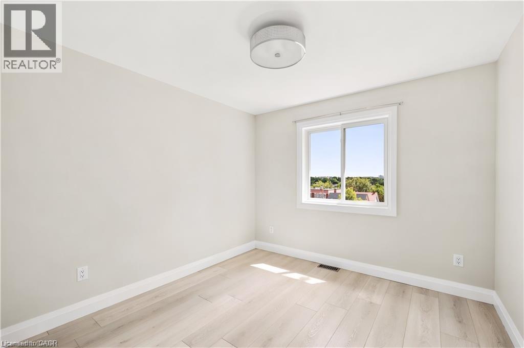 Light-filled room featuring wood-finish flooring, neutral wall tones, and a window with white trim - 129 St George Street, Kitchener, ON