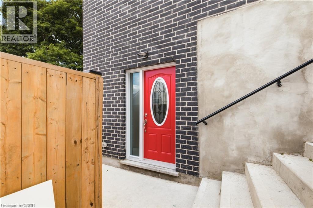 Vibrant red entry door with an oval glass insert, framed by dark brick siding and a natural wood fence - 129 St George Street, Kitchener, ON