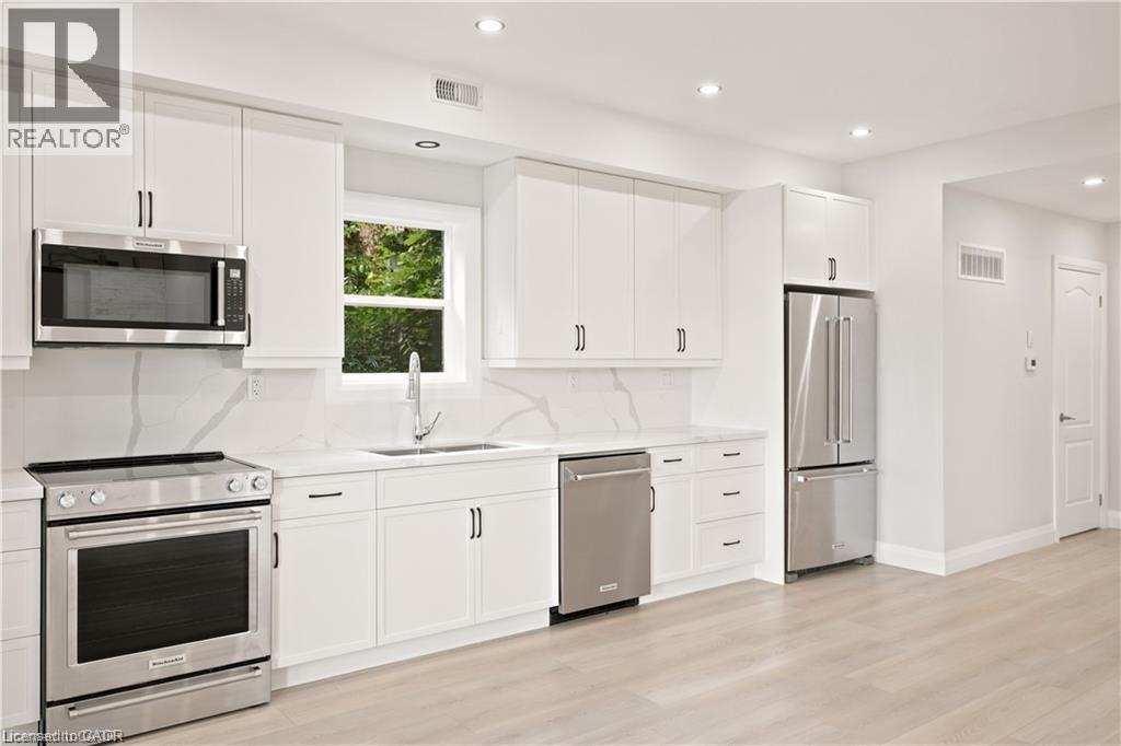 Bright kitchen featuring white cabinetry, stainless steel appliances, a single basin sink, and wood-finish flooring - 129 St George Street, Kitchener, ON