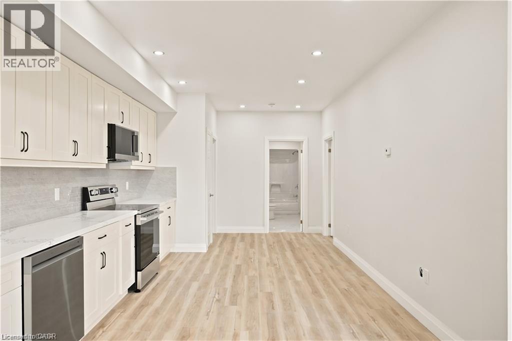 Kitchen featuring light wood-finish flooring, white cabinetry with black hardware, stainless steel appliances, and recessed lighting - 129 St George Street, Kitchener, ON