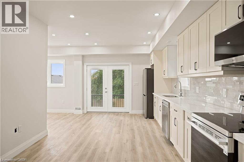 Open concept kitchen featuring light wood-finish flooring, white cabinetry with dark hardware, a white countertop, and a tiled backsplash - 129 St George Street, Kitchener, ON
