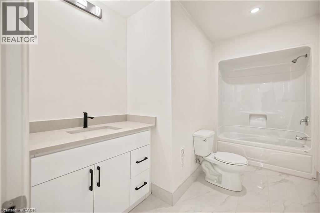Bathroom featuring white cabinetry with matte black hardware, a light-toned countertop with integrated sink, a matte black faucet, and a combination tub/shower unit - 129 St George Street, Kitchener, ON