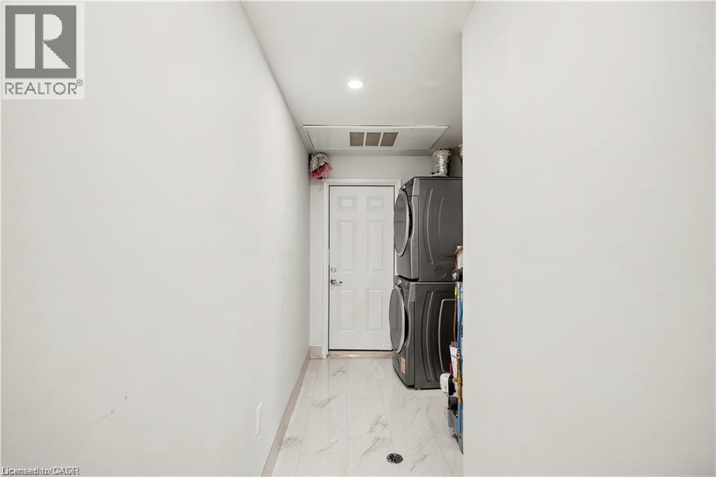 Dedicated laundry area featuring stacked appliances, a white panel door, light-toned flooring, and recessed lighting - 129 St George Street, Kitchener, ON