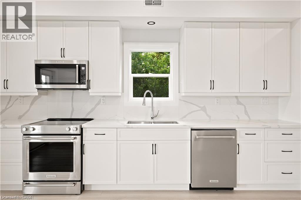 Contemporary kitchen featuring white shaker cabinetry, stainless steel appliances, a white farmhouse sink, and stone countertops with a matching backsplash - 129 St George Street, Kitchener, ON
