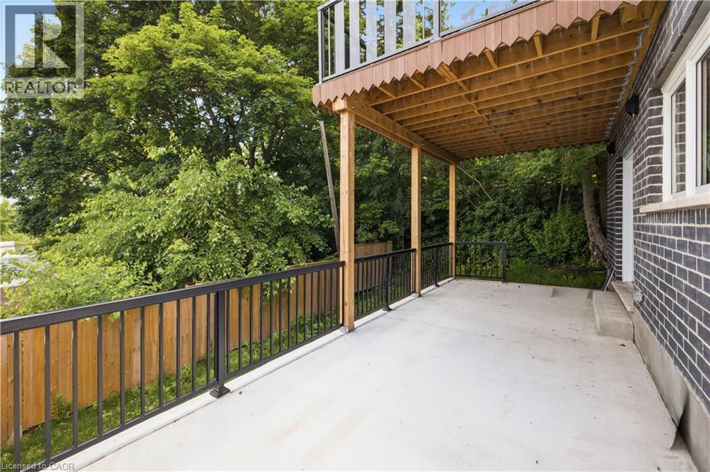 Spacious covered concrete patio with black metal railings and a wooden privacy fence - 129 St George Street, Kitchener, ON