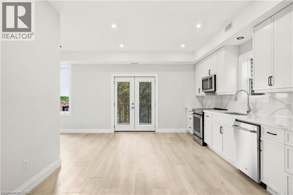Open-concept kitchen featuring white cabinetry, stainless steel appliances, and light wood-finish flooring - 129 St George Street, Kitchener, ON