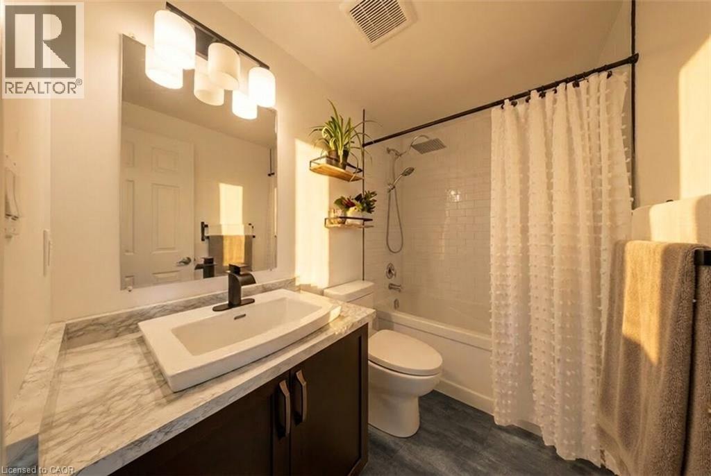 Bathroom featuring a dark wood-finish vanity with a vessel sink, a marble-patterned countertop, and matte black fixtures - 30 Imperial Road S Unit# 21, Guelph, ON