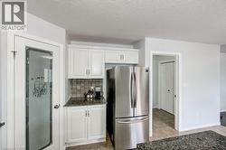 Kitchen area featuring white cabinetry, a stainless steel refrigerator, granite-style countertops, and a tile backsplash -