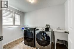 Dedicated laundry area featuring tile flooring, white walls, and a utility sink -