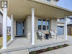 Stone facade residence with a covered porch featuring white support columns, a gray entry door with transom window, and a gray garage door -