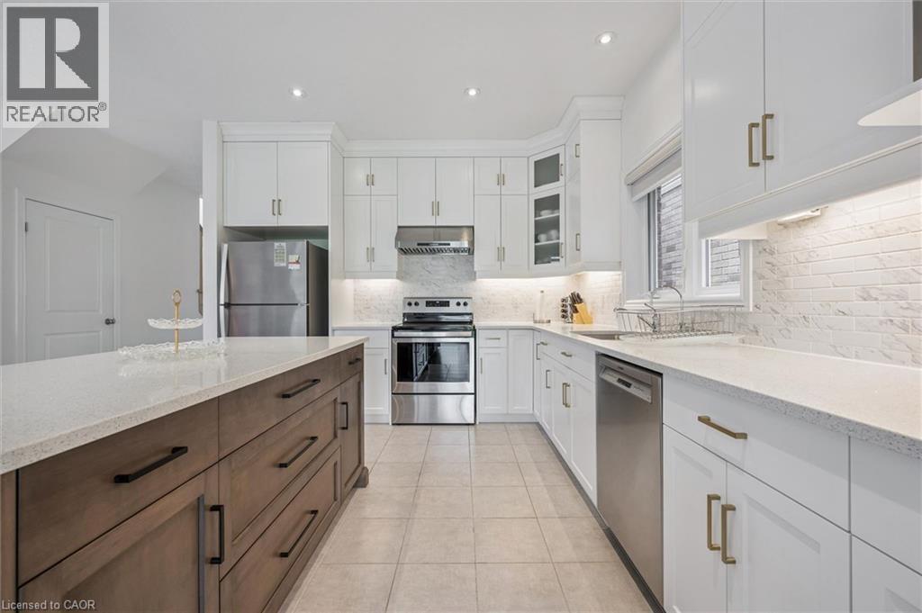 Contemporary kitchen featuring a two-toned island with ample storage, white cabinetry, integrated stainless steel appliances, a tile backsplash, and recessed lighting - 153 Rivertrail Avenue, Kitchener, ON - Indoor Photo Showing Kitchen With Upgraded Kitchen