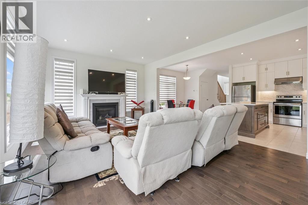 Open-concept living space featuring wood-finish flooring, a contemporary fireplace with mantel, recessed lighting, and a kitchen with white cabinetry, a wood-finish island, and stainless steel applian - 153 Rivertrail Avenue, Kitchener, ON - Indoor Photo Showing Living Room With Fireplace