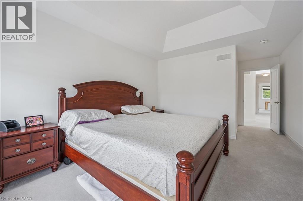Carpeted bedroom featuring a tray ceiling, white walls, and a doorway leading to another area - 153 Rivertrail Avenue, Kitchener, ON - Indoor Photo Showing Bedroom