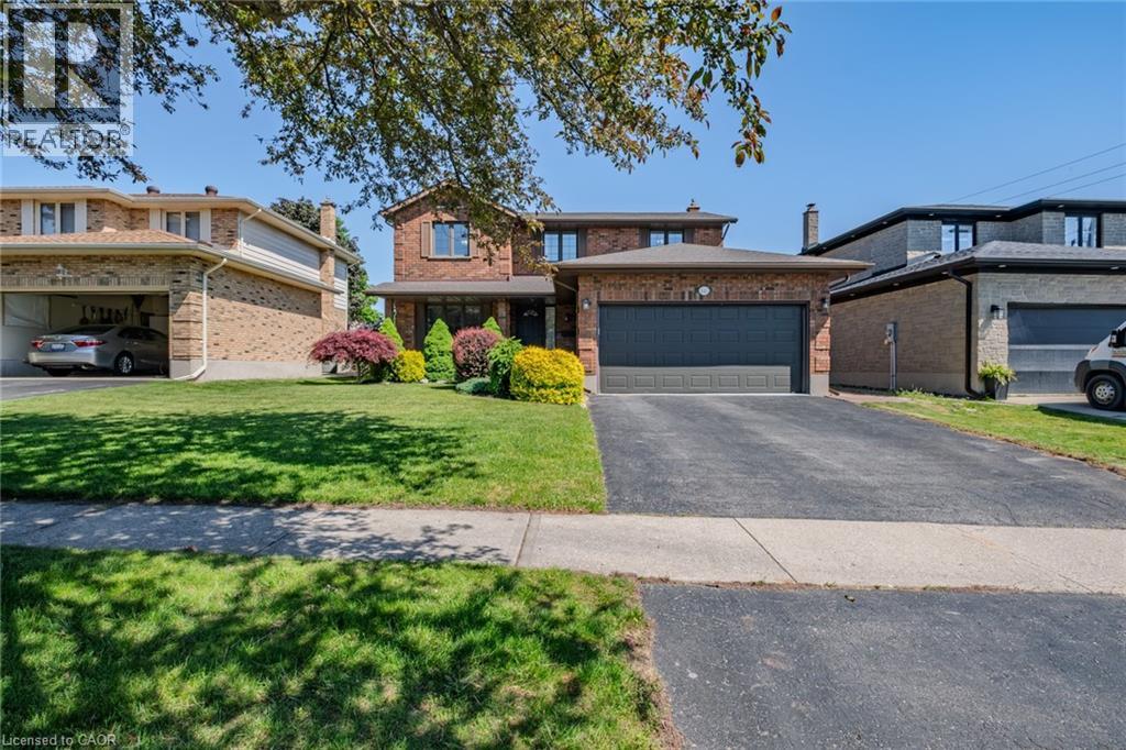 Brick-clad residence featuring an attached two-car garage with a dark panel door, a landscaped front yard with varied shrubbery, and a paved driveway - 141 Lynndale Road, Simcoe, ON