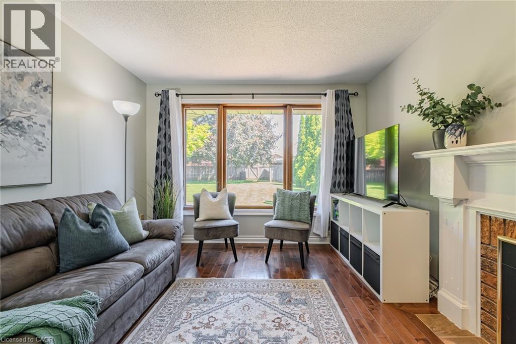 Spacious living area featuring rich wood-finish flooring, a prominent bay window, a classic fireplace with a white mantel, and light-toned wall finishes - 141 Lynndale Road, Simcoe, ON