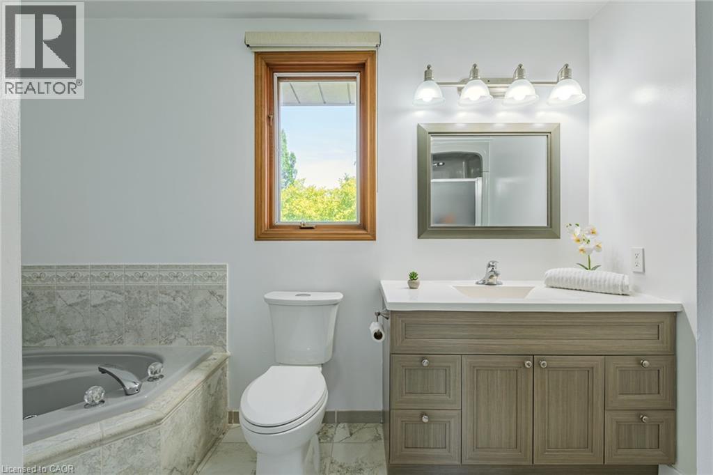 Contemporary bathroom featuring a wood-finish vanity with a light countertop, an undermount sink, and a framed mirror - 141 Lynndale Road, Simcoe, ON