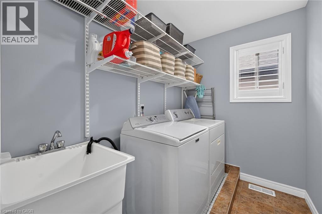 Dedicated laundry area featuring a utility sink with chrome faucet, overhead adjustable wire shelving, and a window with white shutters - 43 Wilbur Drive, Binbrook, ON