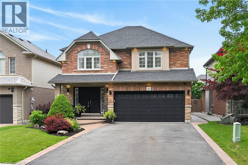 Brick exterior with stone accents, a two-car garage, and a paved driveway with stone border - 43 Wilbur Drive, Binbrook, ON