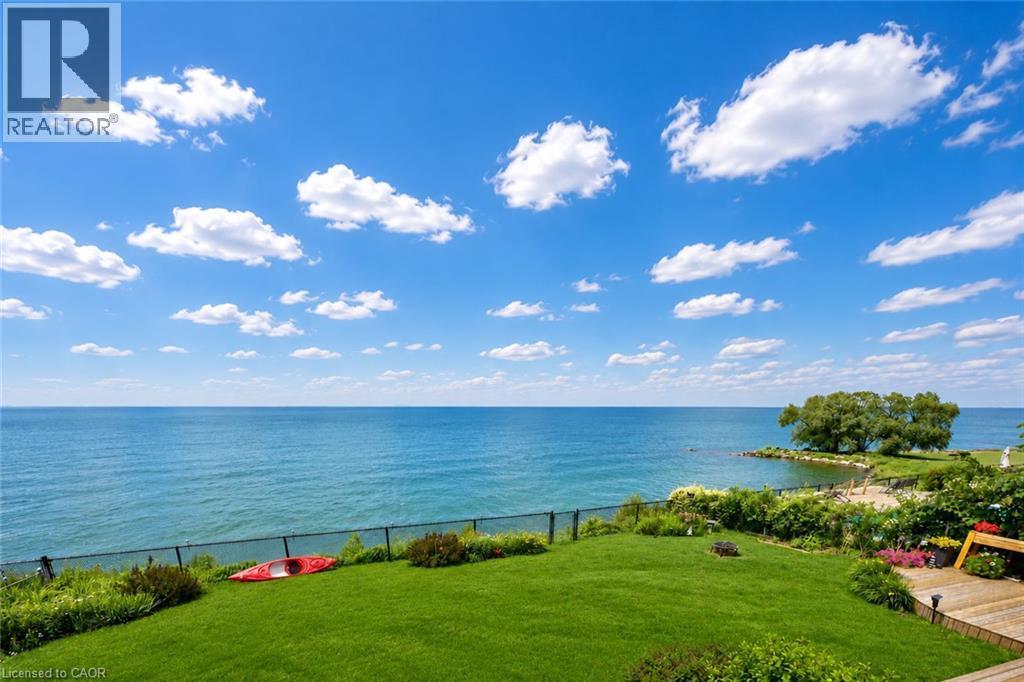 Expansive waterfront property featuring a manicured lawn, lush landscaping, and a secure perimeter fence - 15 Cheval Drive, Grimsby, ON - Outdoor With Body Of Water With View