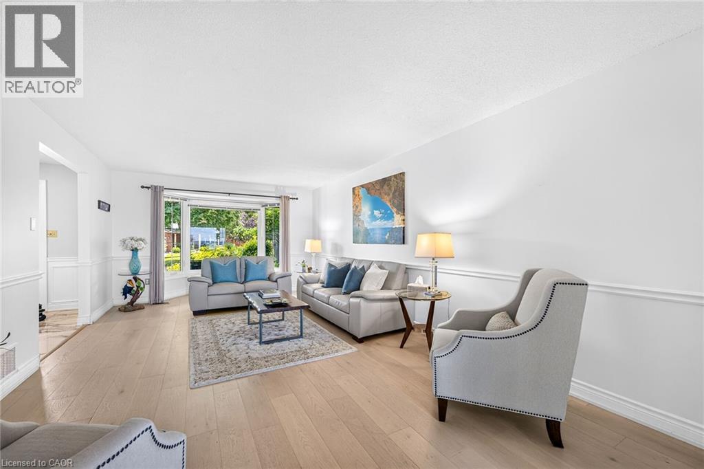 Bright living area featuring wood-finish flooring, white wainscoting, and a large bay window - 15 Cheval Drive, Grimsby, ON - Indoor Photo Showing Living Room