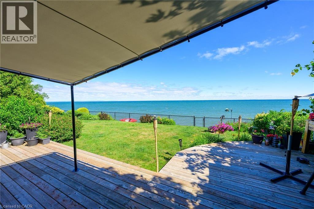 Expansive wood deck with a partial shade awning, featuring a manicured lawn and mature landscaping - 15 Cheval Drive, Grimsby, ON - Outdoor With Body Of Water With Deck Patio Veranda With View With Exterior