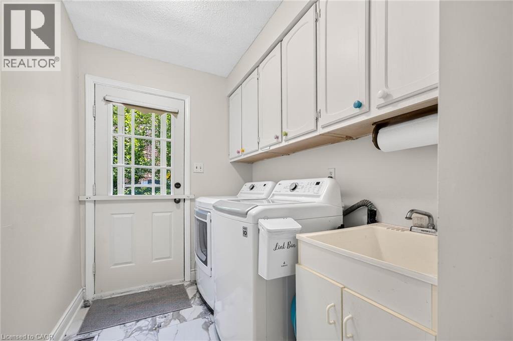 Dedicated laundry room featuring white cabinetry, a utility sink, and durable marble-look flooring - 15 Cheval Drive, Grimsby, ON - Indoor Photo Showing Laundry Room