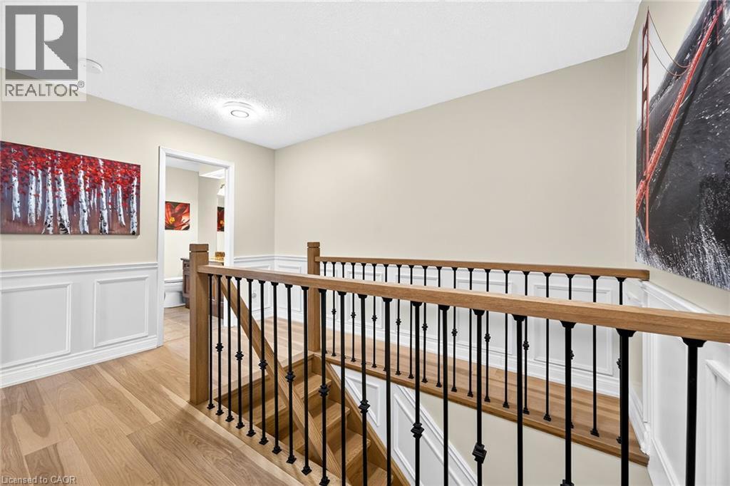 Upper-level hallway featuring wood-finish flooring, wainscoting, and a staircase with wood handrails and black metal balusters - 15 Cheval Drive, Grimsby, ON - Indoor Photo Showing Other Room
