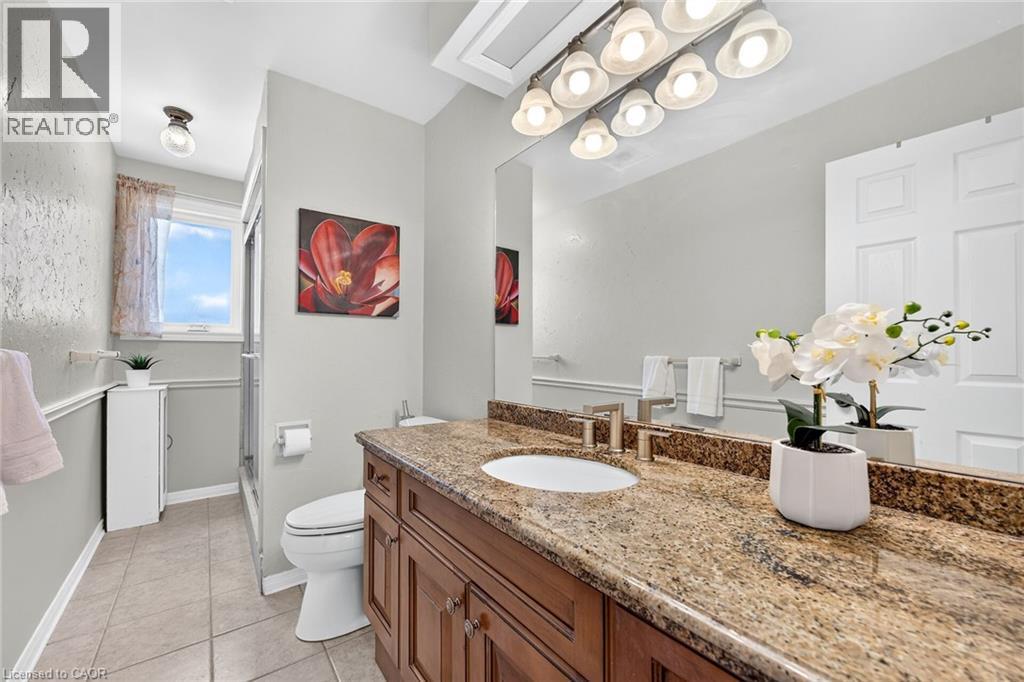 Bathroom featuring a dual-sink vanity with a granite countertop, wood-finish cabinetry, and brushed nickel fixtures - 15 Cheval Drive, Grimsby, ON - Indoor Photo Showing Bathroom