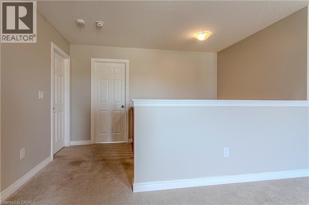 Upper-level hallway featuring neutral wall paint, white trim, two paneled doors, and a partial railing - 3896 Tufgar Crescent, Burlington, ON