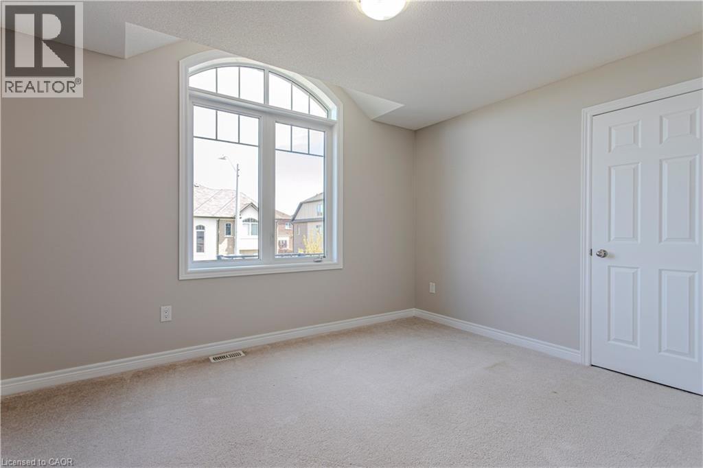 Room featuring a large arched window, neutral wall paint, white trim, and light-colored carpeting - 3896 Tufgar Crescent, Burlington, ON