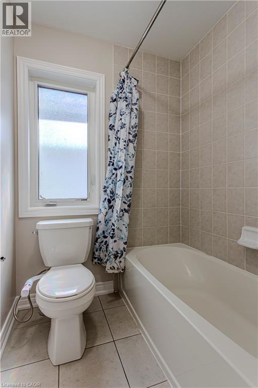 Bathroom featuring a white bathtub, ceramic wall tiling, and a window with frosted glass - 3896 Tufgar Crescent, Burlington, ON
