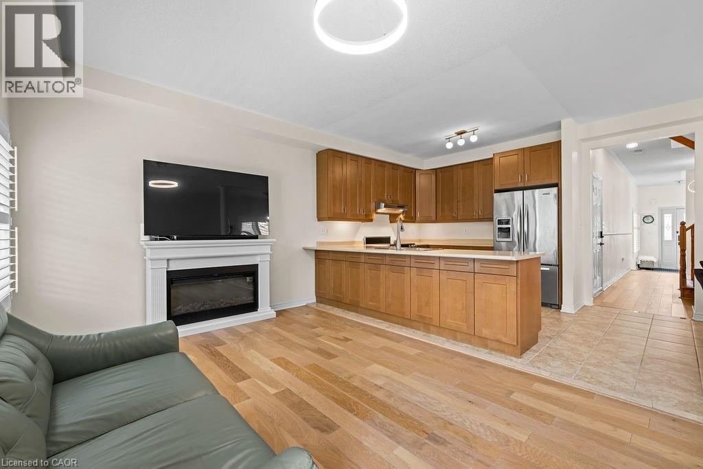Open-concept living area with light wood-finish flooring, a contemporary fireplace with a white mantel, and a kitchen featuring wood cabinetry, light countertops, and stainless steel appliances - 4670 Thomas Alton Boulevard, Burlington, ON