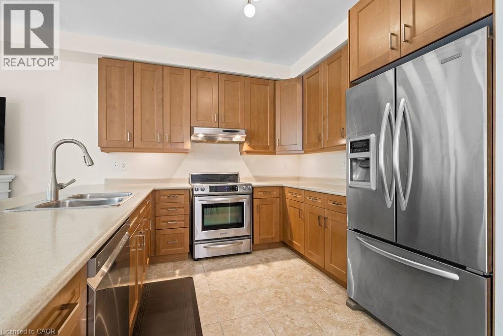 Kitchen featuring light wood cabinetry, light-toned countertops, tile flooring, and stainless steel appliances including a refrigerator, range, and dishwasher - 4670 Thomas Alton Boulevard, Burlington, ON