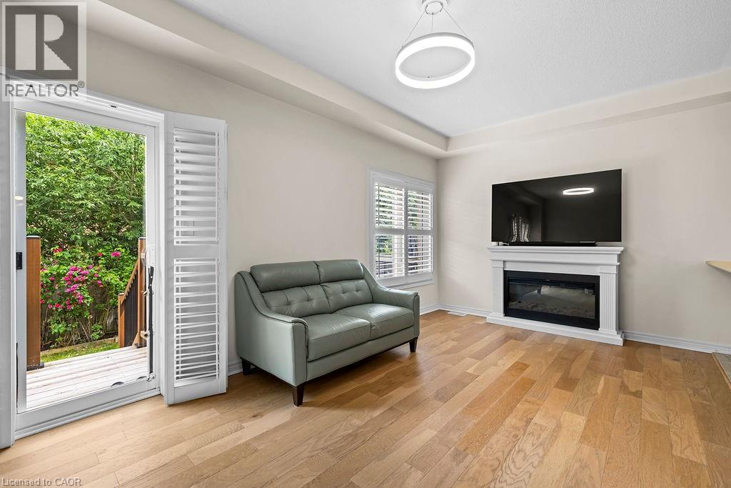 Living area featuring wood-finish flooring, a contemporary fireplace with a white mantel, and a sliding glass door leading to a wooden deck - 4670 Thomas Alton Boulevard, Burlington, ON