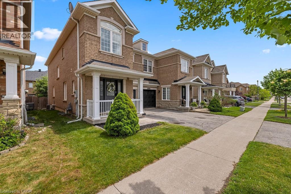 Brick and stone facade townhome featuring a covered porch with white columns and railing - 4670 Thomas Alton Boulevard, Burlington, ON