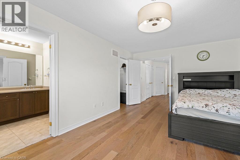 Bedroom featuring wood-finish flooring, a contemporary drum light fixture, and an open doorway revealing an attached bathroom - 4670 Thomas Alton Boulevard, Burlington, ON