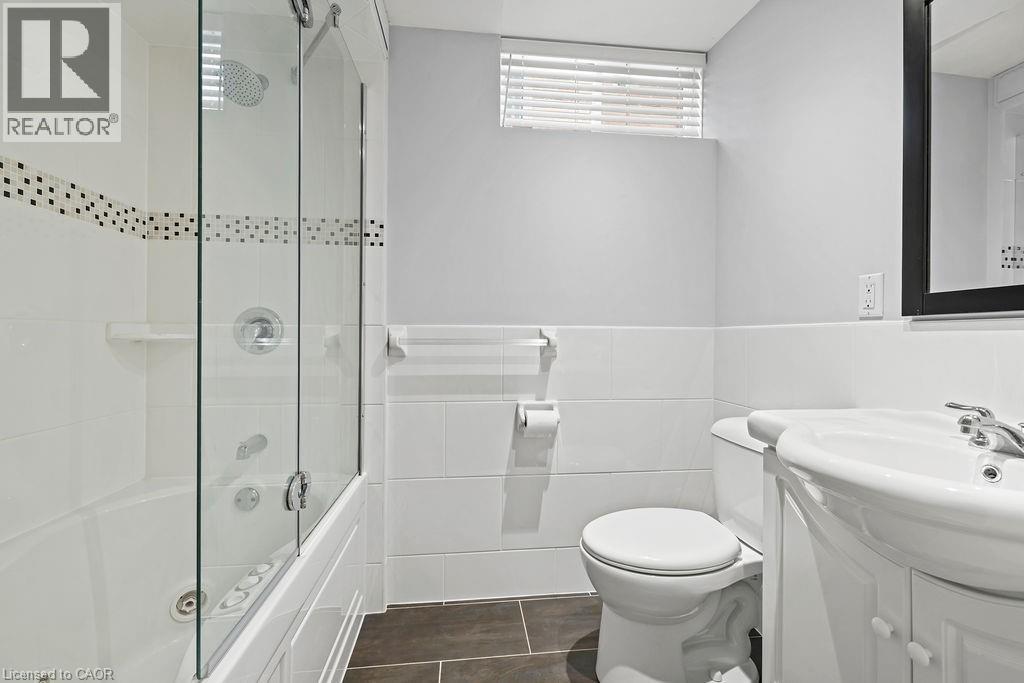 Bathroom featuring a jetted tub with glass shower enclosure, white tile surround with decorative accent, a pedestal vanity, and dark tile flooring - 4670 Thomas Alton Boulevard, Burlington, ON