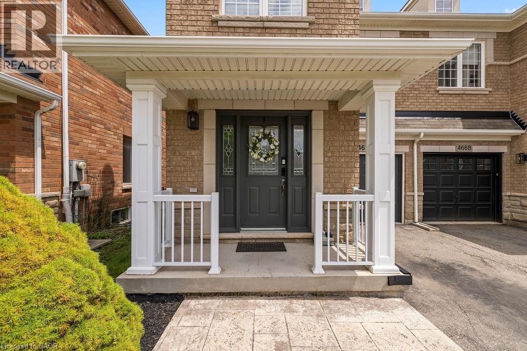 Covered front porch with white columns and railings, featuring a dark gray door with decorative glass inserts - 4670 Thomas Alton Boulevard, Burlington, ON