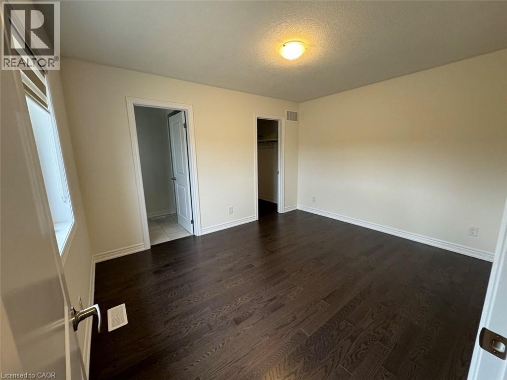 Spacious room featuring dark wood-finish flooring, light neutral-toned walls, and white baseboards - 10 Guernsey Drive Unit# Upper, Kitchener, ON