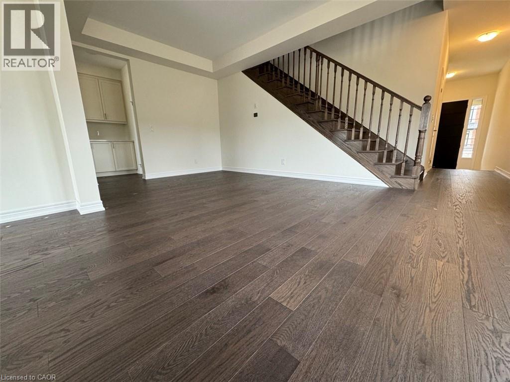 Expansive room featuring wide plank wood-finish flooring, a grand staircase with dark wood banister and balusters, a tray ceiling, and a built-in cabinetry niche - 10 Guernsey Drive Unit# Upper, Kitchener, ON
