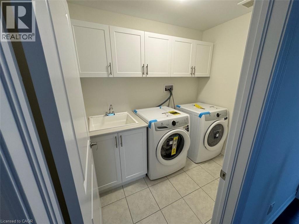 Laundry area featuring white shaker-style cabinetry, a utility sink, and light-toned tile flooring - 10 Guernsey Drive Unit# Upper, Kitchener, ON